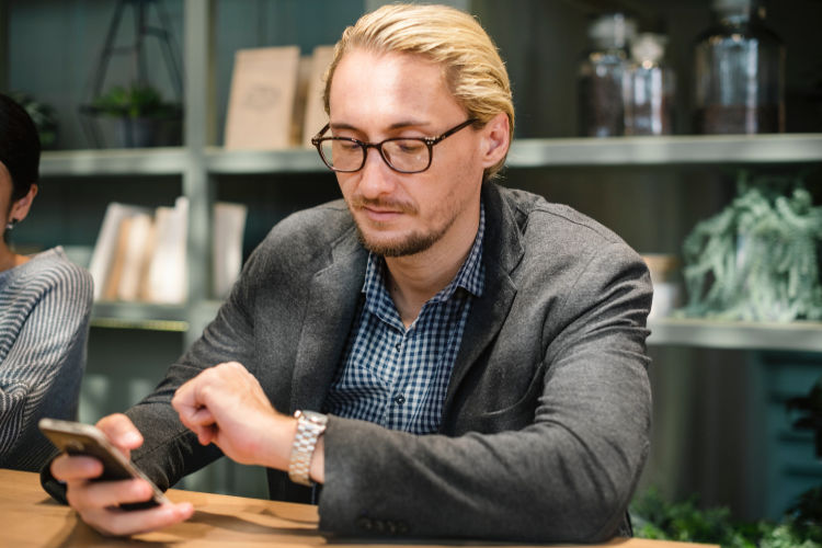 A man looking at his watch and a smartphone